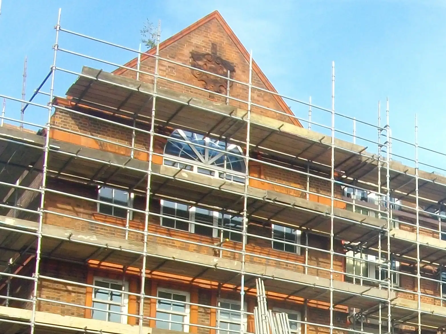 Scaffolding up to the decorated gable end and arched window of a Victorian school in Camberley