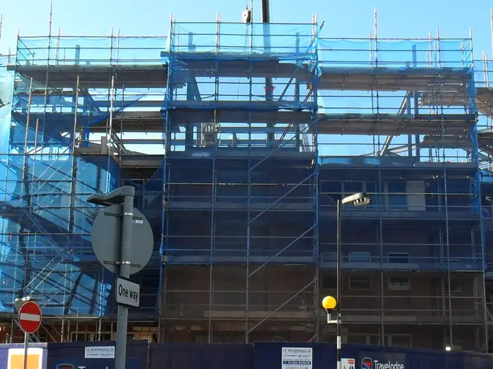 Netted scaffold lifts rising above the frame of a new hotel in Guildford