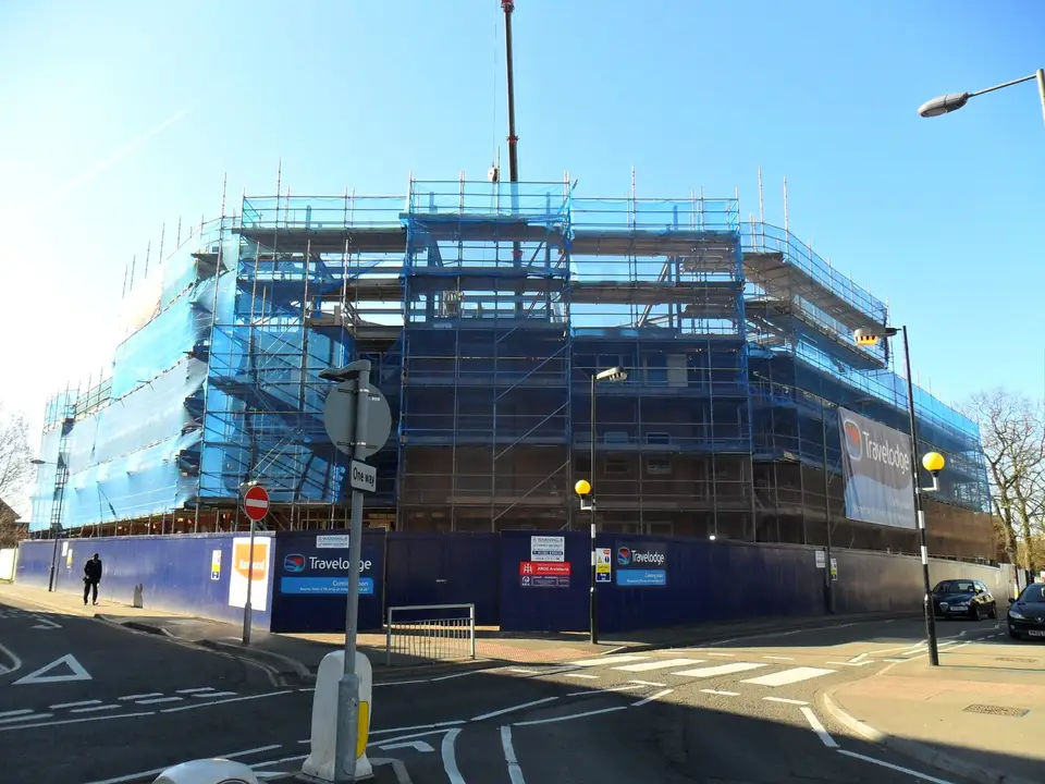 Netted scaffold on a new hotel under construction in Guildford town centre, behind site hoardings